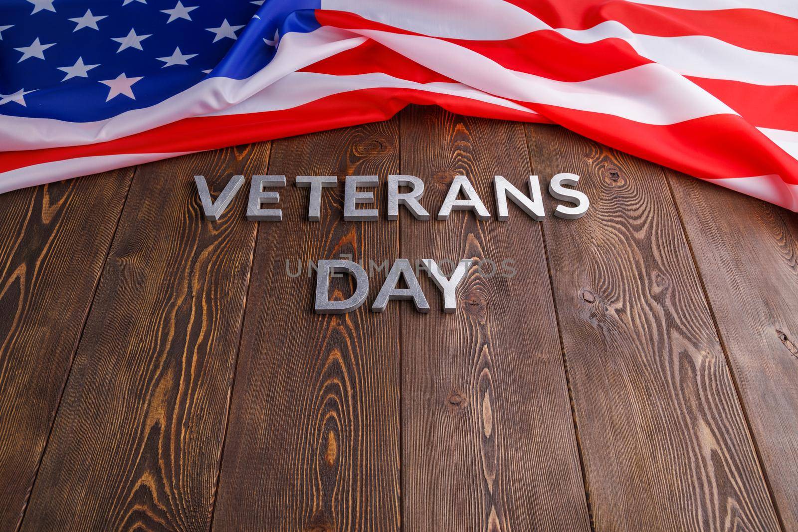 the words veterans day laid with silver metal letters on wooden board surface with crumpled usa flag.
