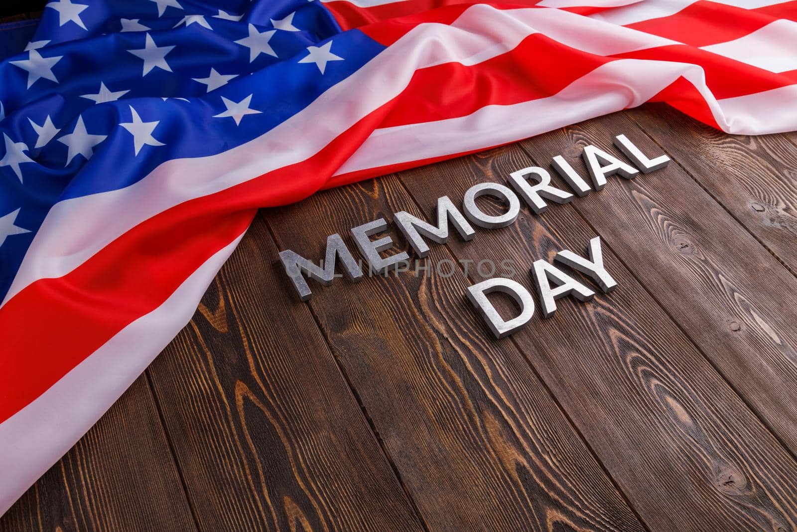 the words memorial day laid with silver metal letters on wooden board surface with crumpled usa flag below with diagonal perspective