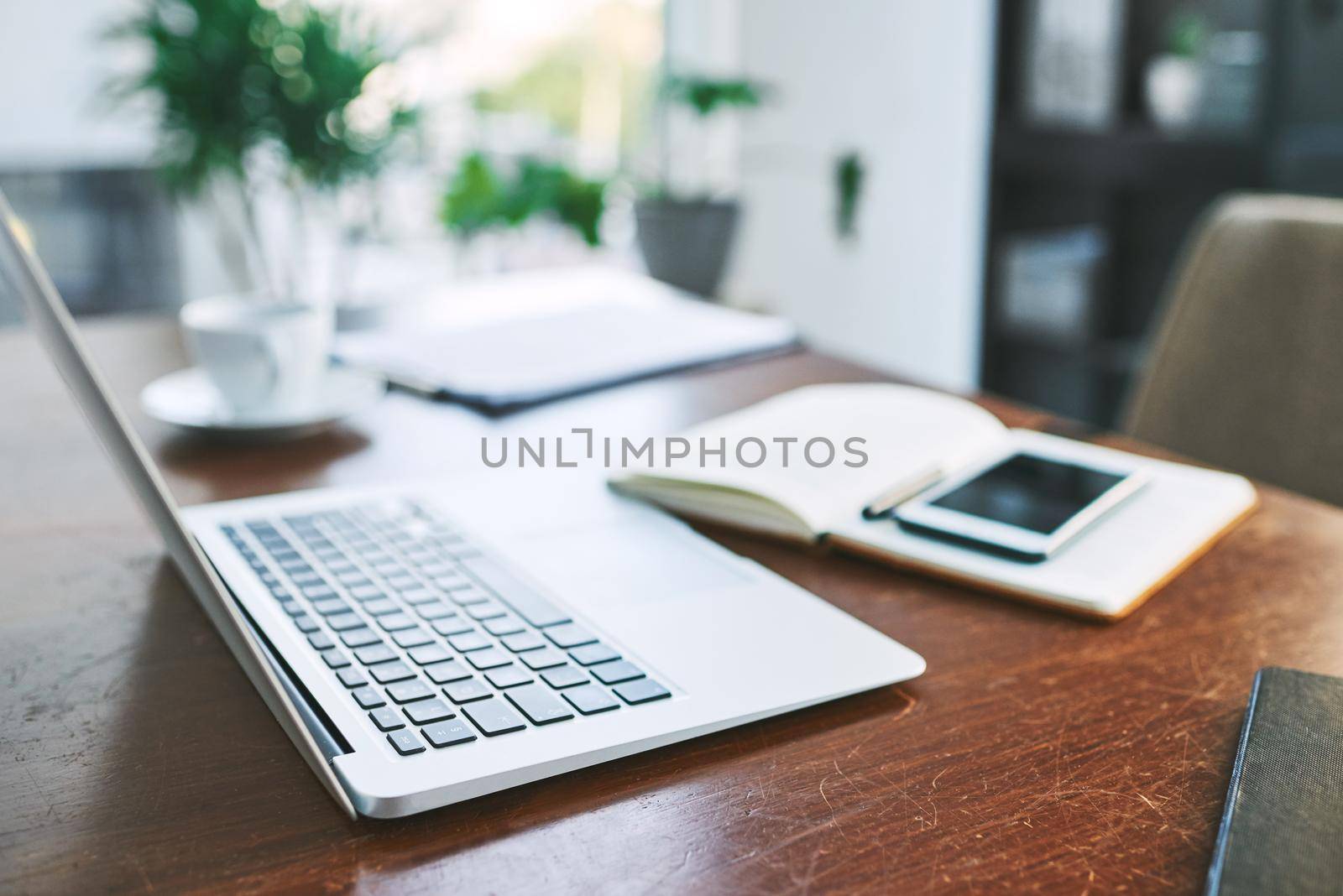 Lets get to work then. Still life shot of a laptop, notebook and cellphone on a table in an office. by YuriArcurs