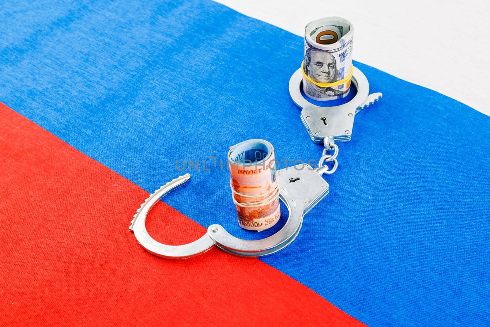 roll of us dollar banknotes in a handcuffs with a roll of russian ruble banknotes on flat full-frame russian flag background, closeup