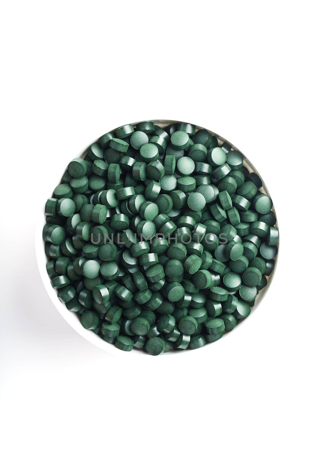 Spirulina tablets in a white cup on a white background by AlexGrec