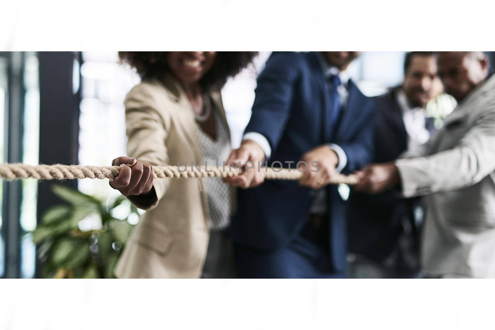 Challenges can be overturned with teamwork. Closeup shot of a group of unrecognizable businesspeople pulling together on a rope in an office. by YuriArcurs