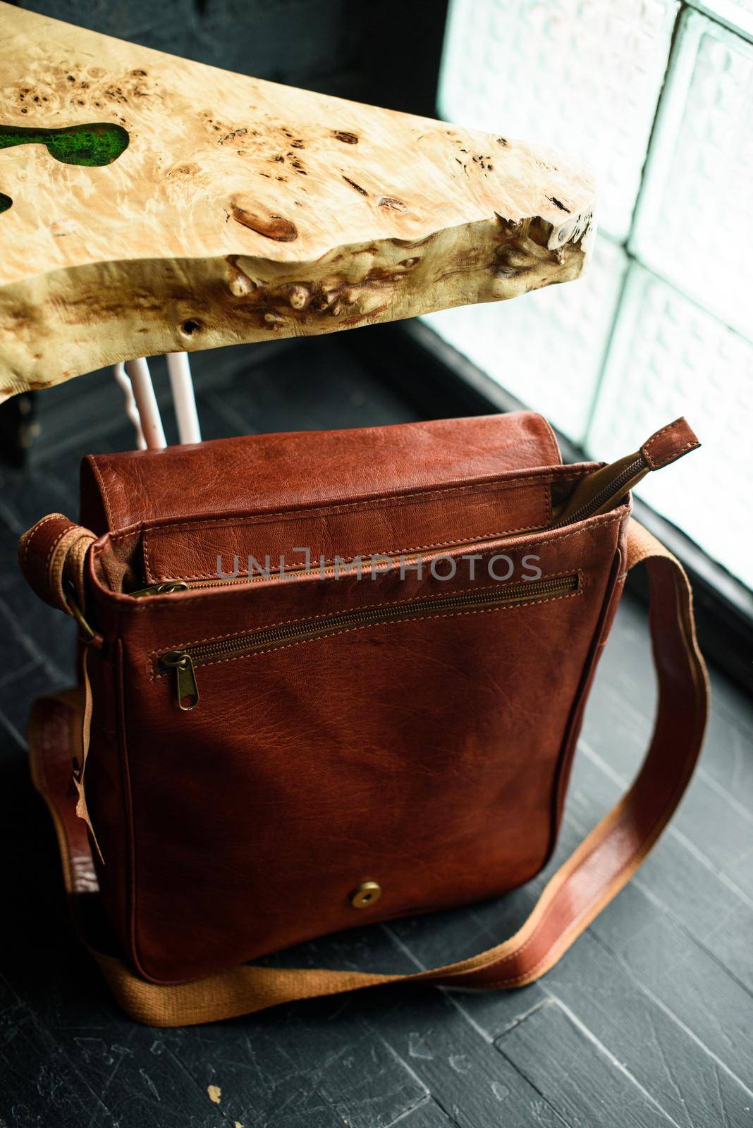 close-up photo of orange leather messanger bag on a wooden table. indoor photo