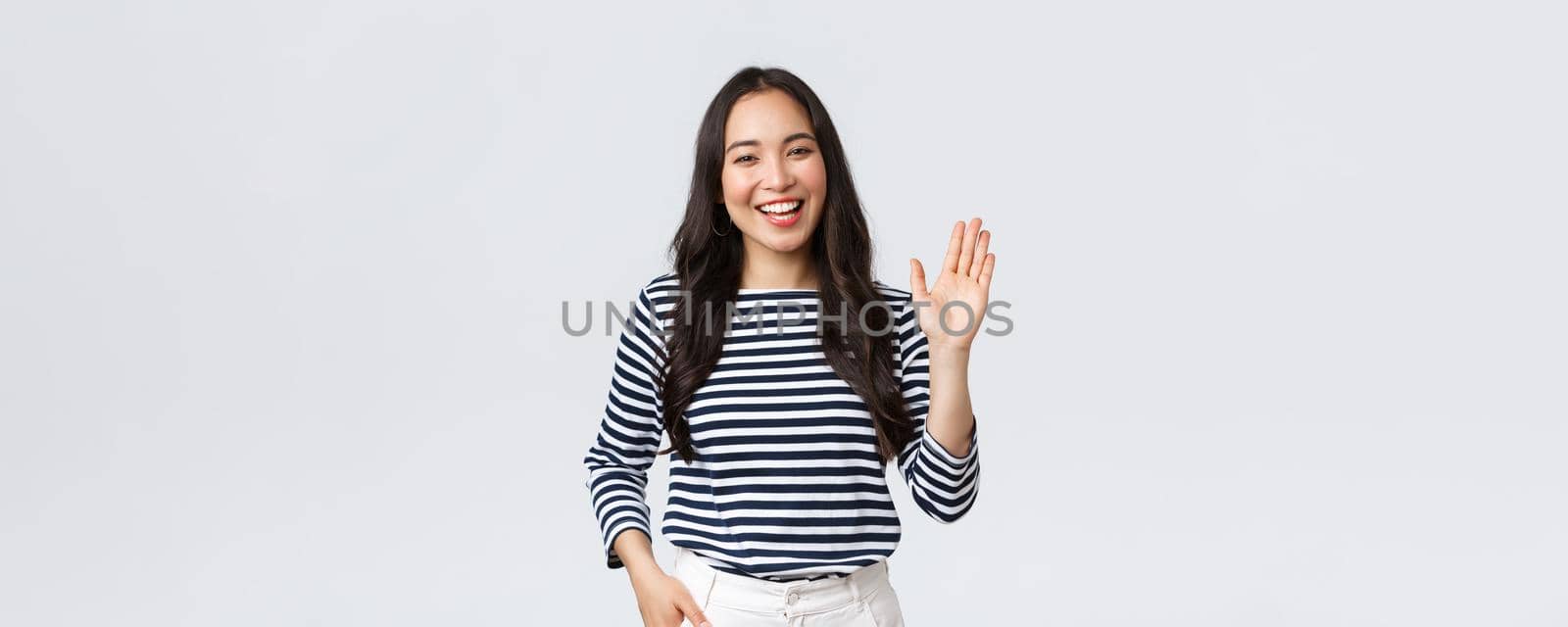 Lifestyle, people emotions and casual concept. Friendly cheerful asian woman smiling, saying hi and waving hand to greet person, make hello gesture, welcome someone.