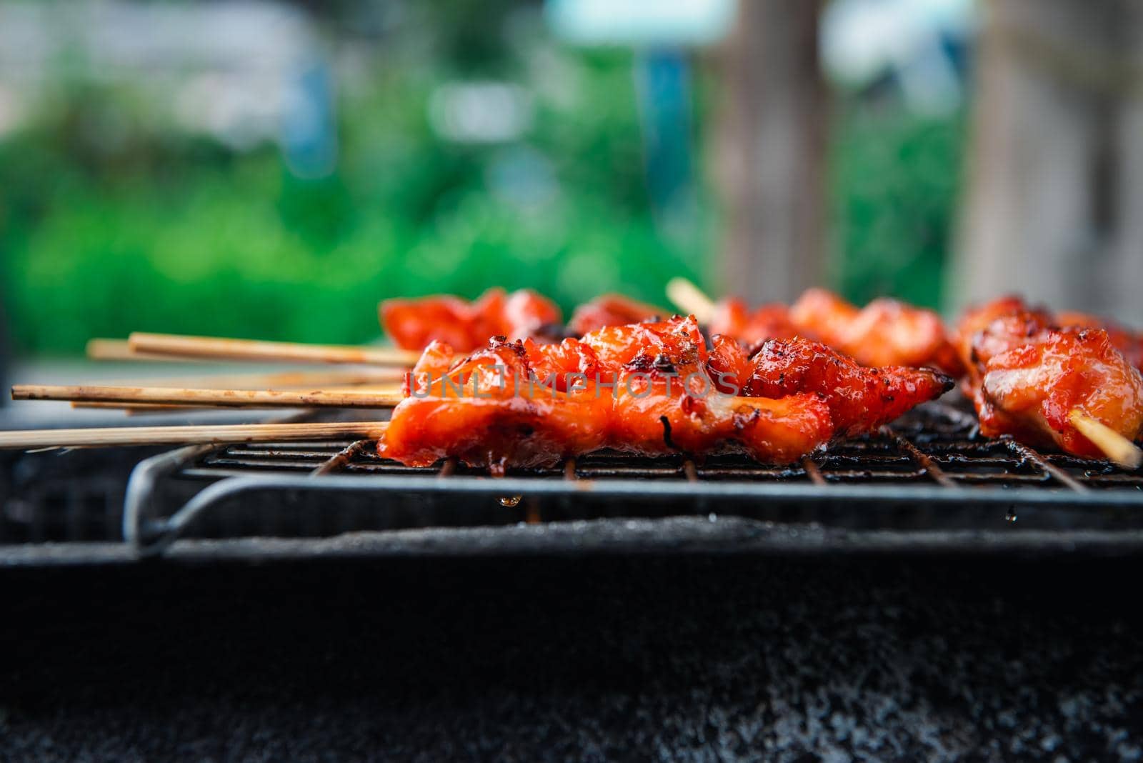 Grilled chicken sauce is a Thai barbeque food by chicken and sauce cooking on charcoal with flames at Thai street food market