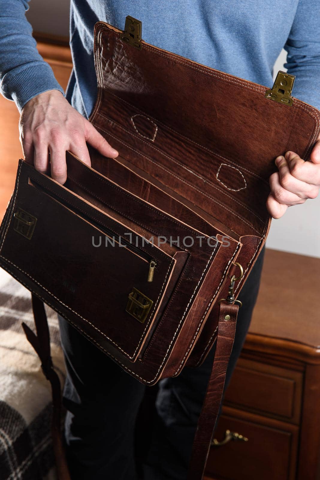 Details of open empty brown men's shoulder leather bag for a documents and laptop on the shoulders of a man in a blue shirt . mens leather handmade briefcase.