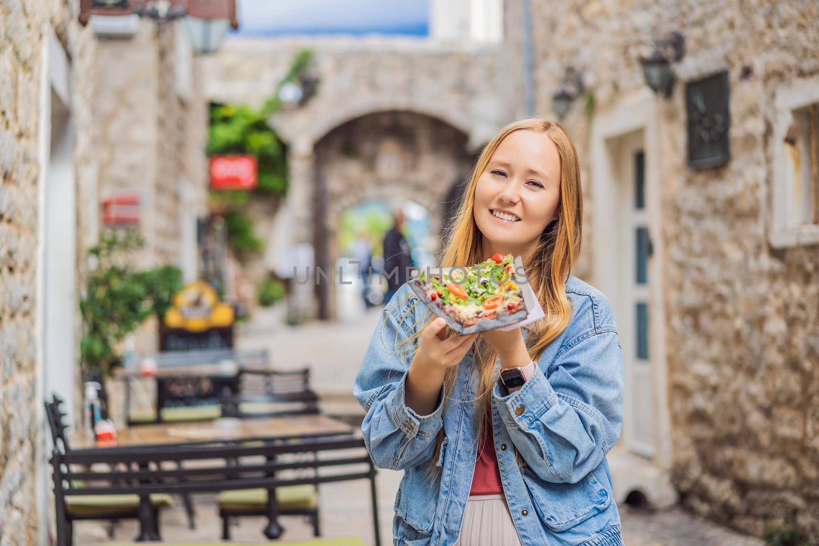 Young woman tourist eating traditional pizza in the old town of Budva. Travel to Montenegro concept by galitskaya