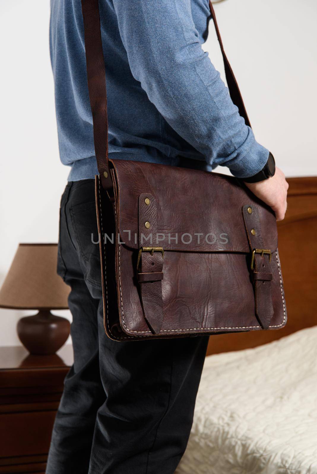 Side view of man in a blue sweater with brown leather briefcase. Retro style. Unisex bag for sale. Indoor photo