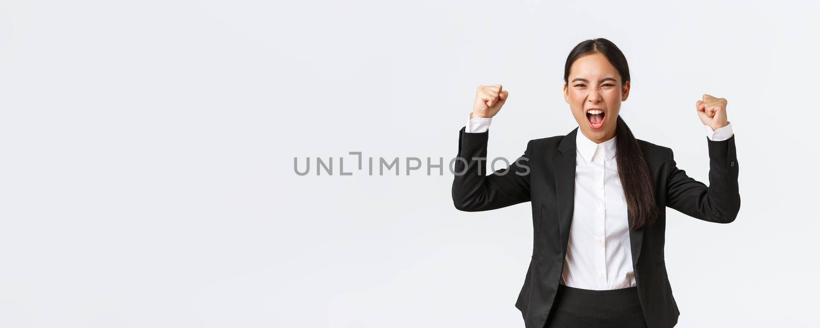 Successful winning businesswoman fist pump and shouting yes from happiness and delighted, achieve goal, celebrating victory, triumphing over prize, standing white background.