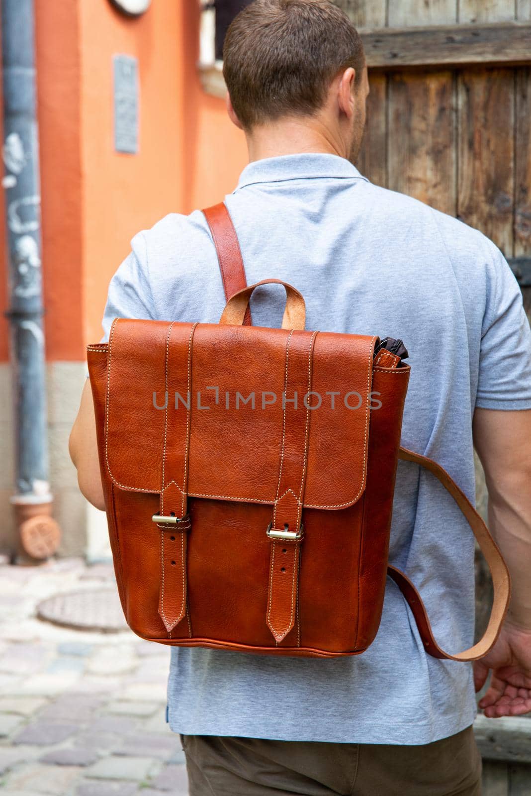 back view of stylish man with leather backpack walking outside.