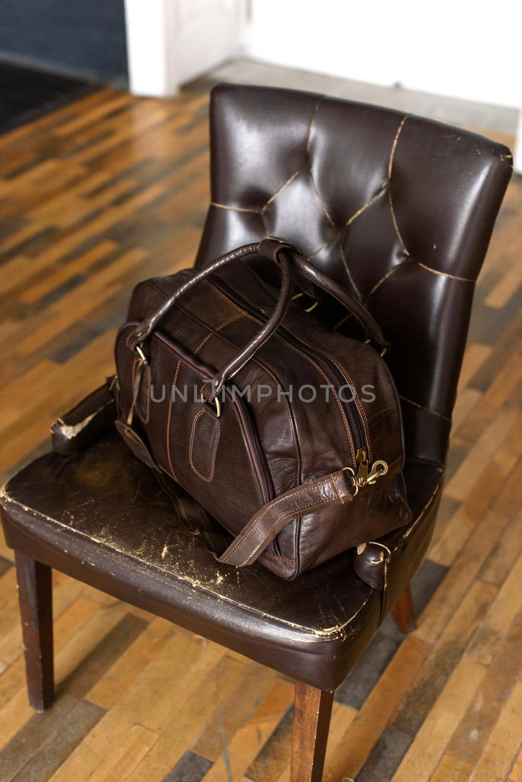 Leather brown travel bag, on a brown leather chair. Indoor photo. soft light