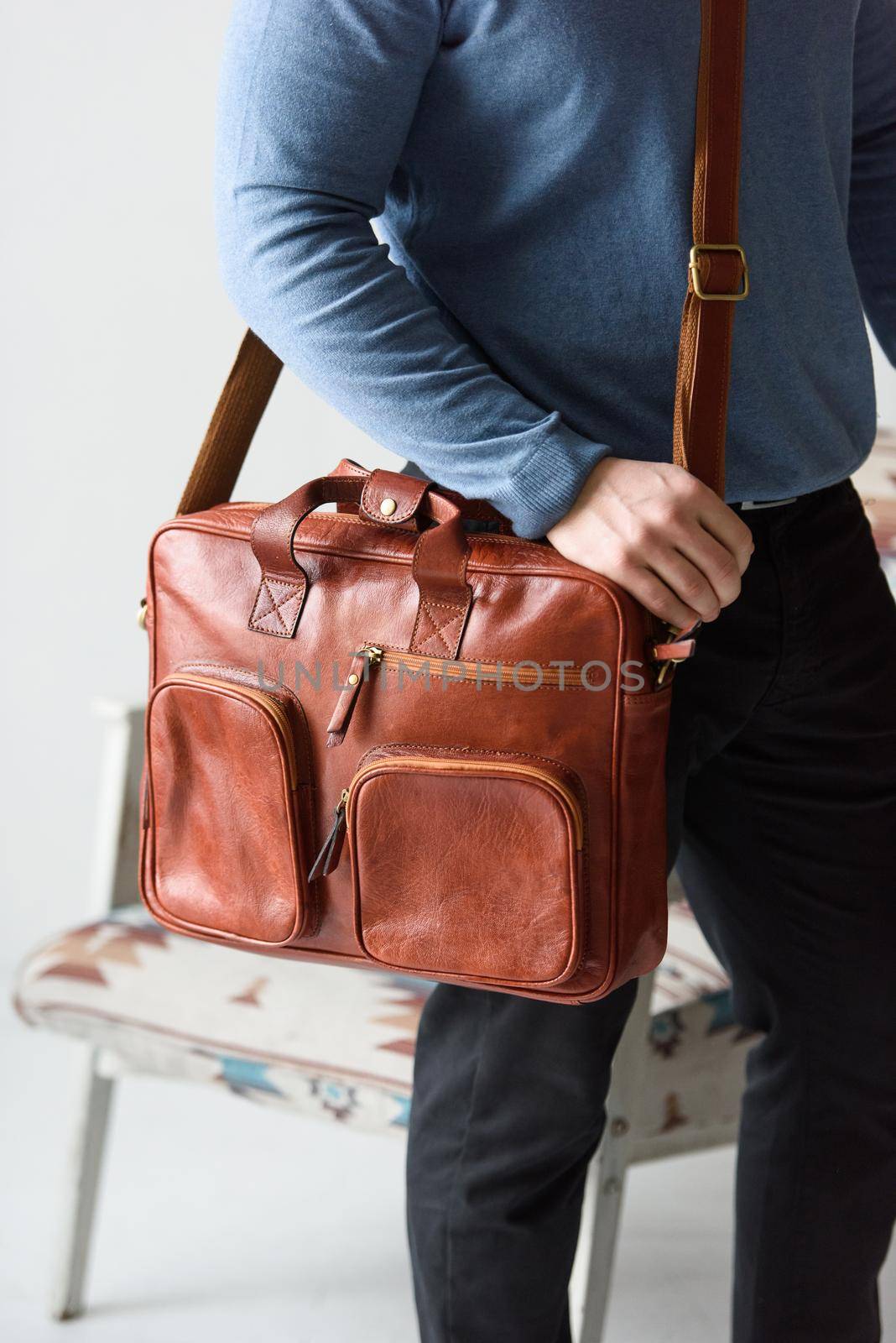 Side view of man in a blue sweater with red leather briefcase. Retro style. Unisex bag for sale. Indoor photo