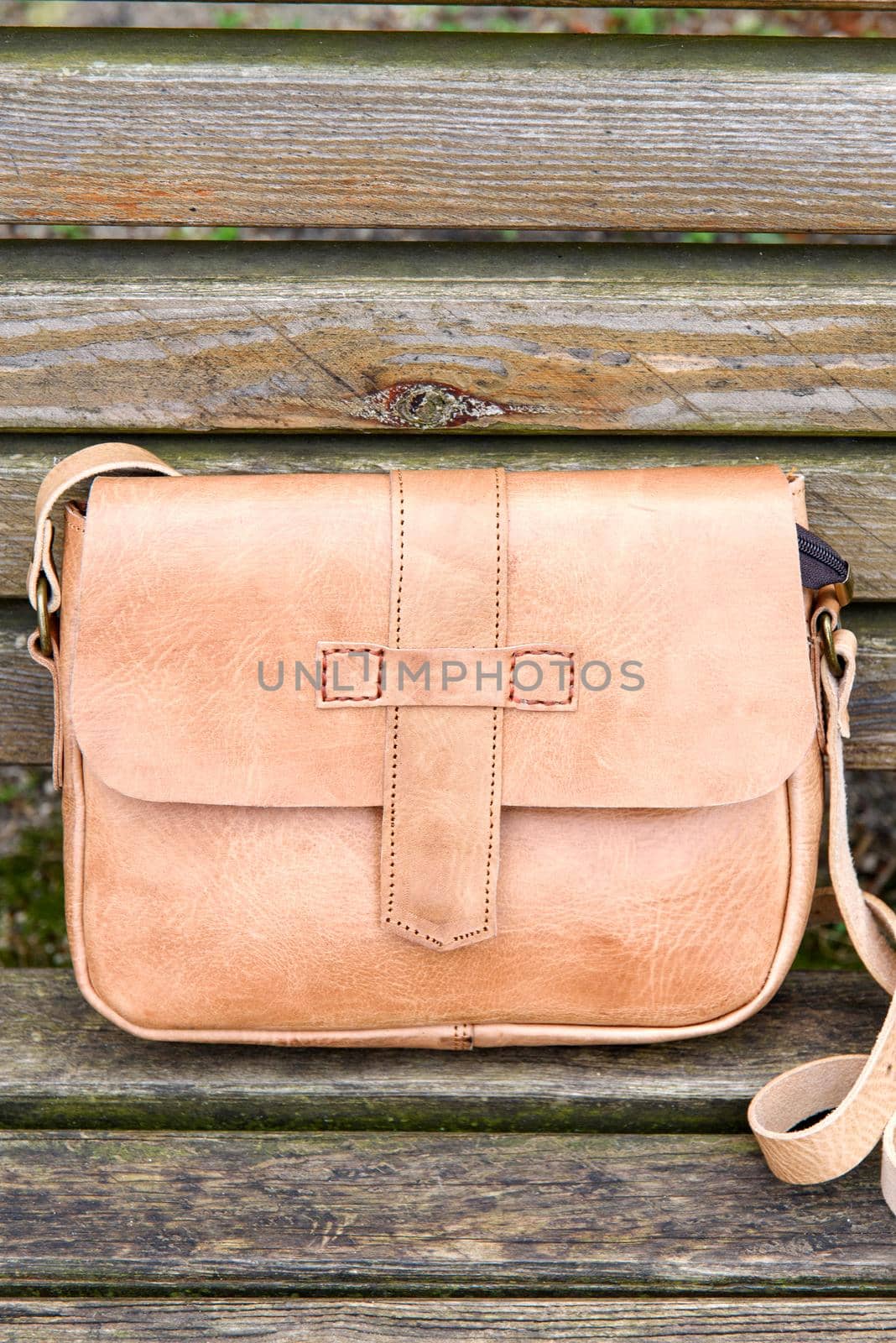 close-up photo of yellow leather handbag on a wooden bench. Outdoors photo