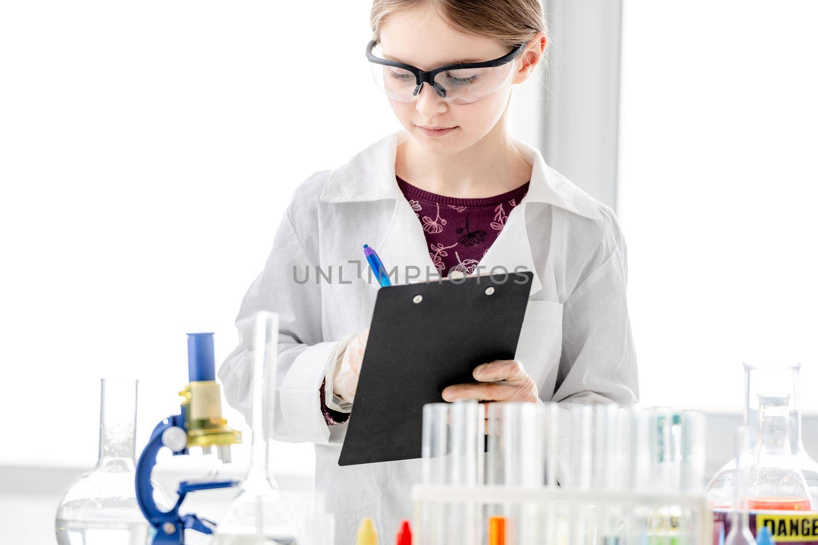 Girl during scientific chemistry experiment making notes close to table with tubes. Schoolgirl with chemical equipment on school lesson