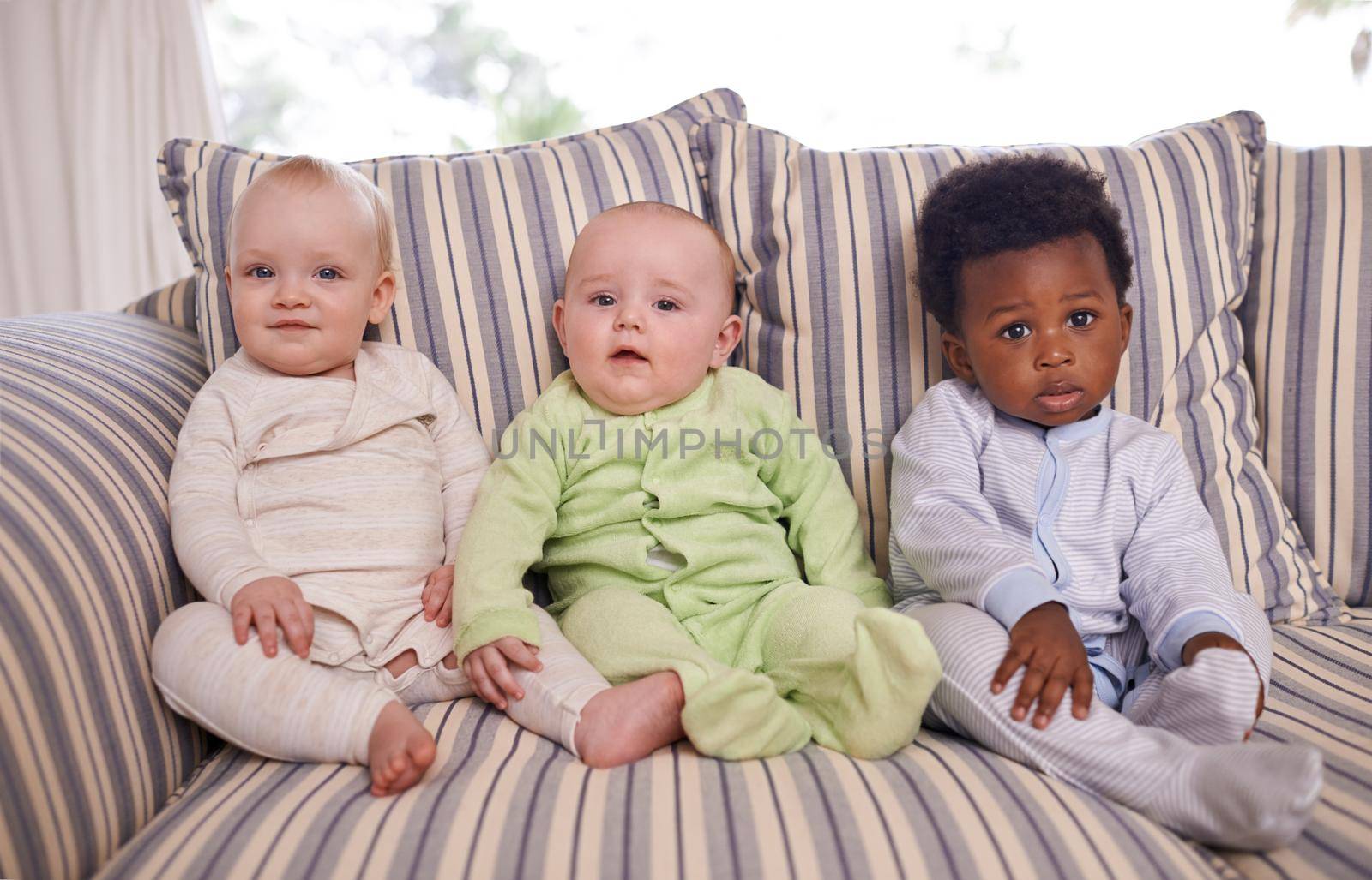 Portrait of three adorable babies sitting on a couch.
