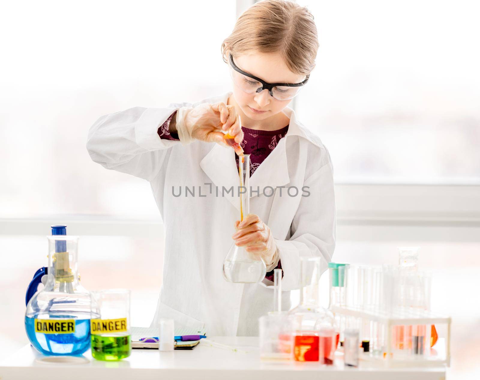 Smart girl during scientific chemistry experiment wearing protection glasses, holding tubes and measuring ingridients. Schoolgirl with chemical equipment on school lesson