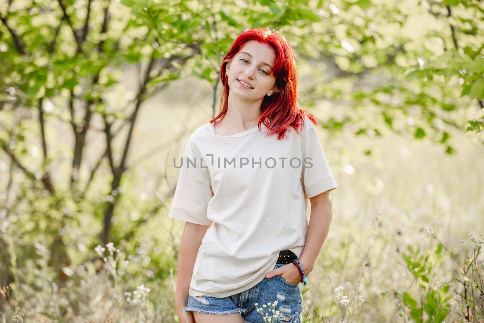 Girl with red hair posing at the nature. Portrait of pretty young female in the sunny field