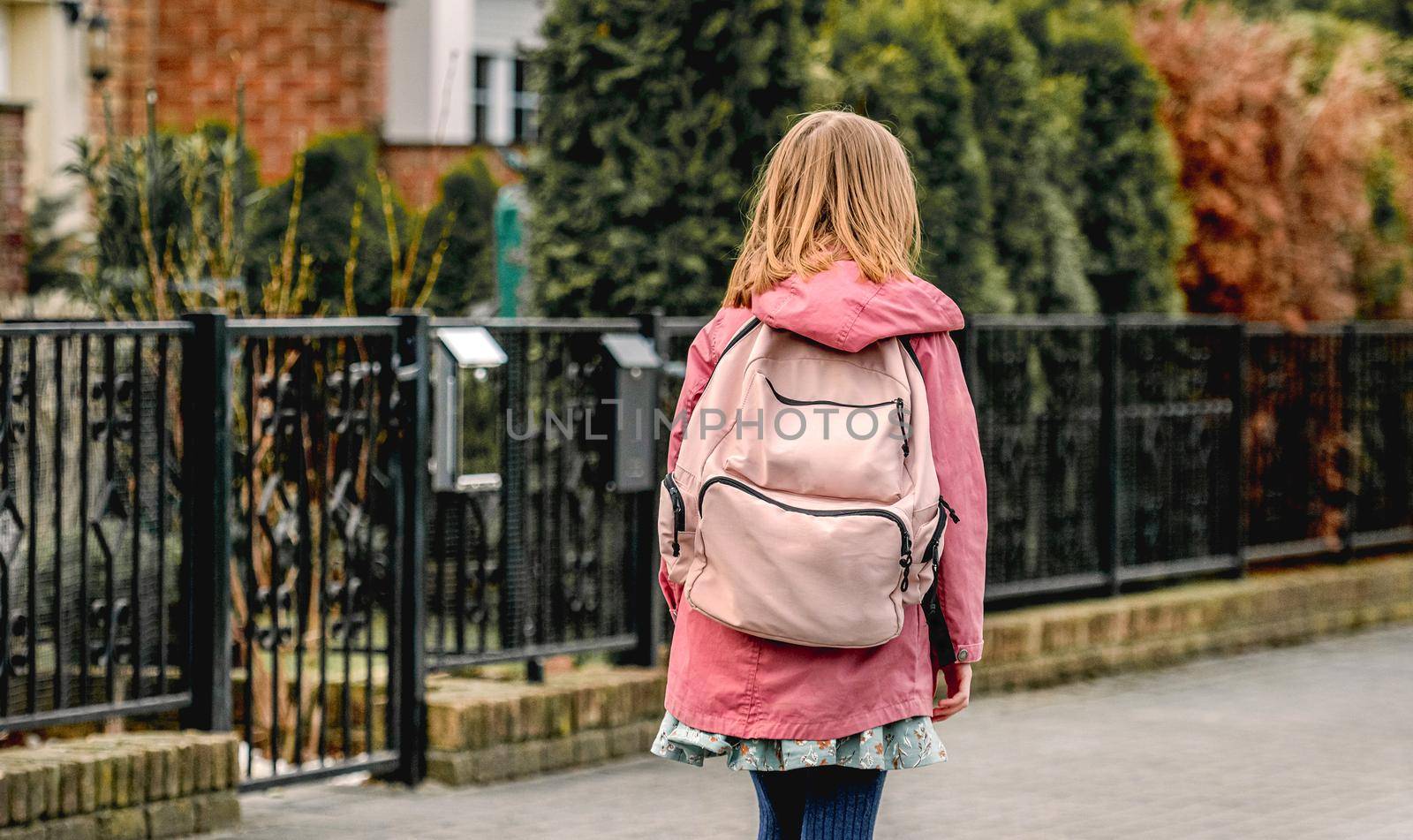 School girl with backpack walks at street. Preteen child kid outdoors after college class, view from back