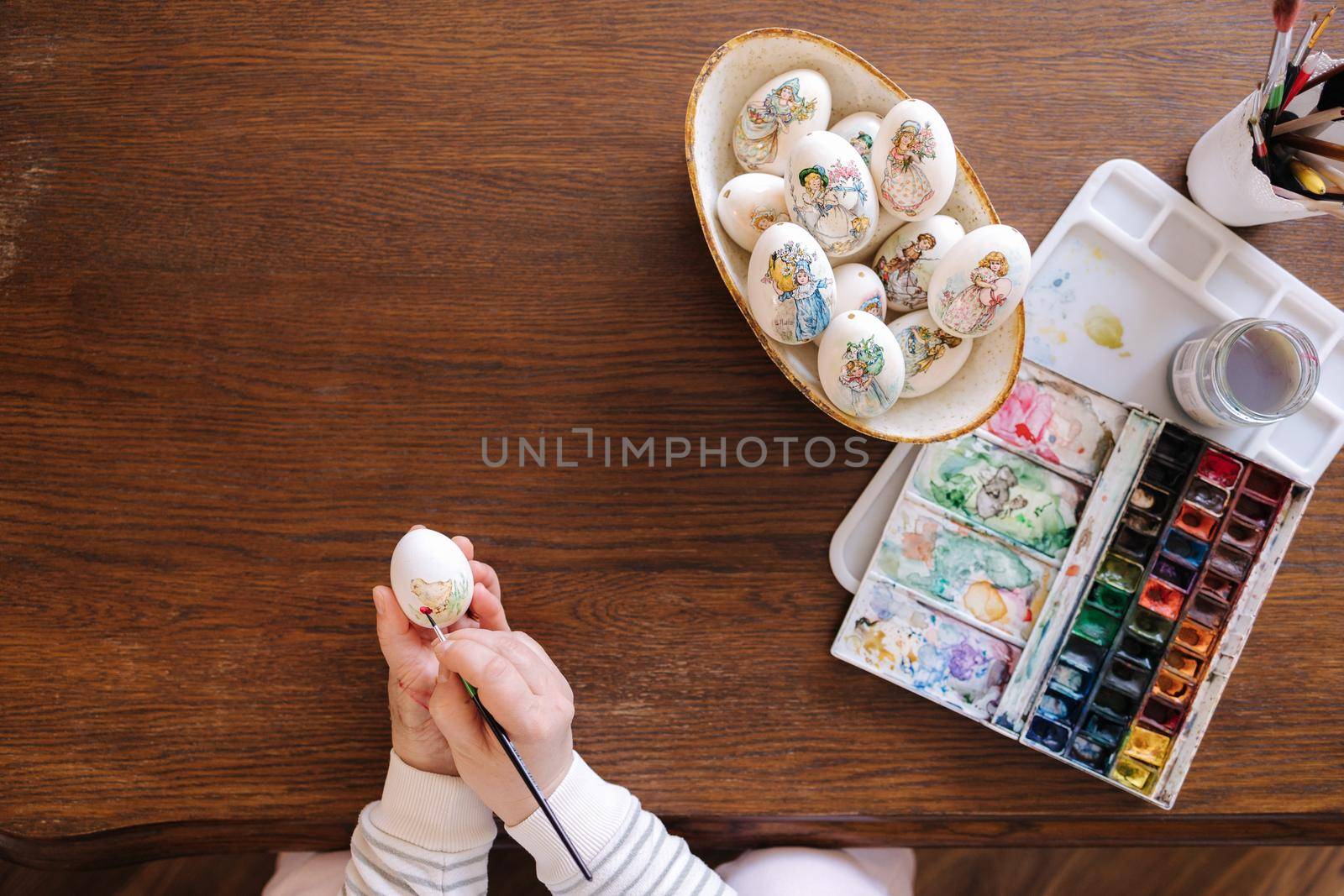 Top view of woman painting a water colors on fantasy chicken eggs for Easter egg festival. Female drawing little yellow chick. The symbolic of spring. Easter concept.
