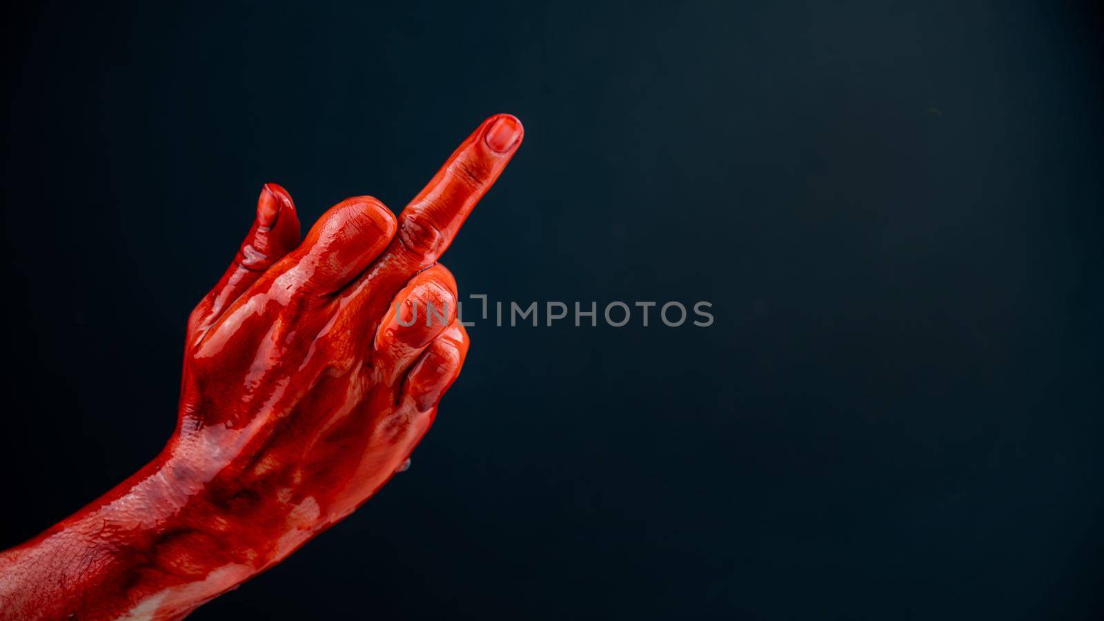 Female hand stained with blood shows the middle finger on a black background