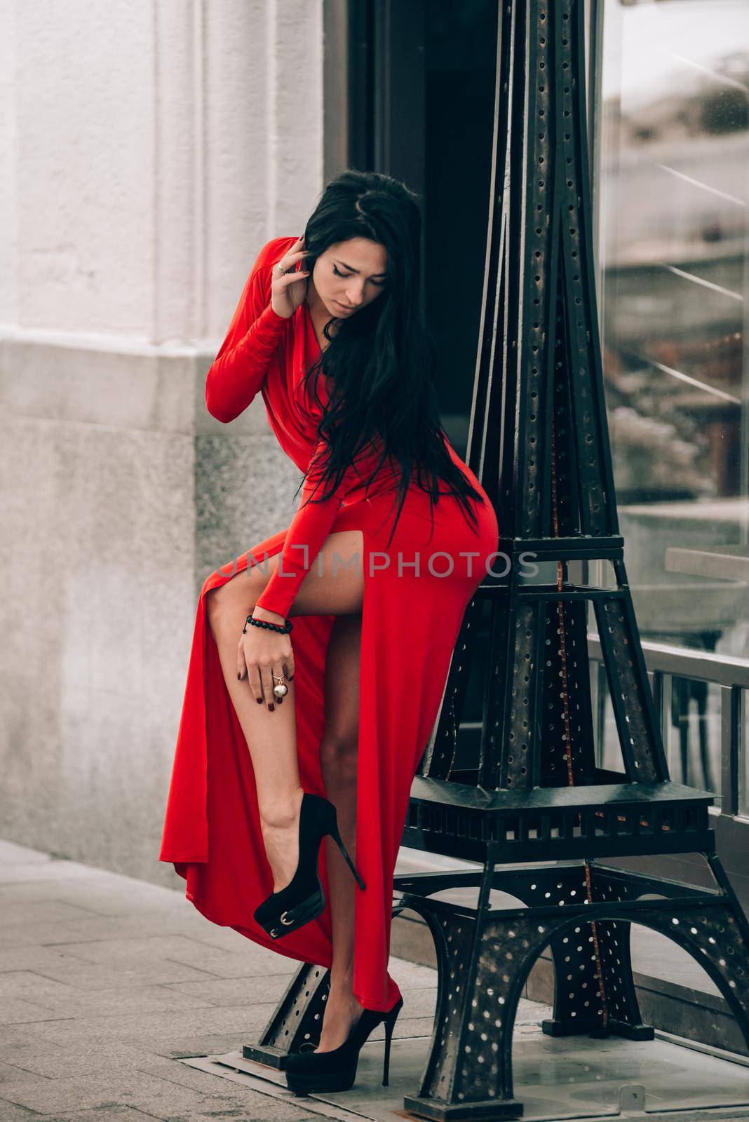 Charming young woman in red sexy dress posing . photo of a seductive woman with black hair near decorative tower. Selective focus