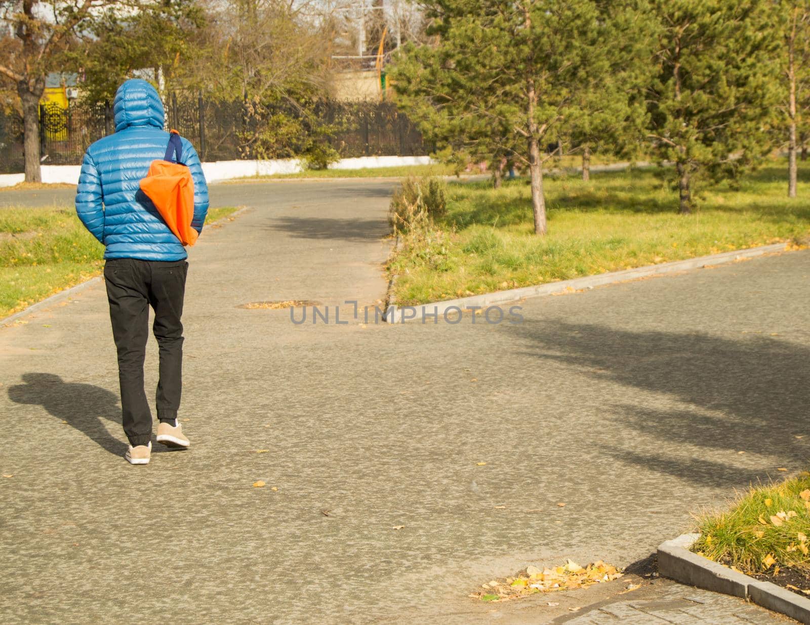 Young handsome man wearing a blue jacket with a sports bag, walking in Park, rear view.