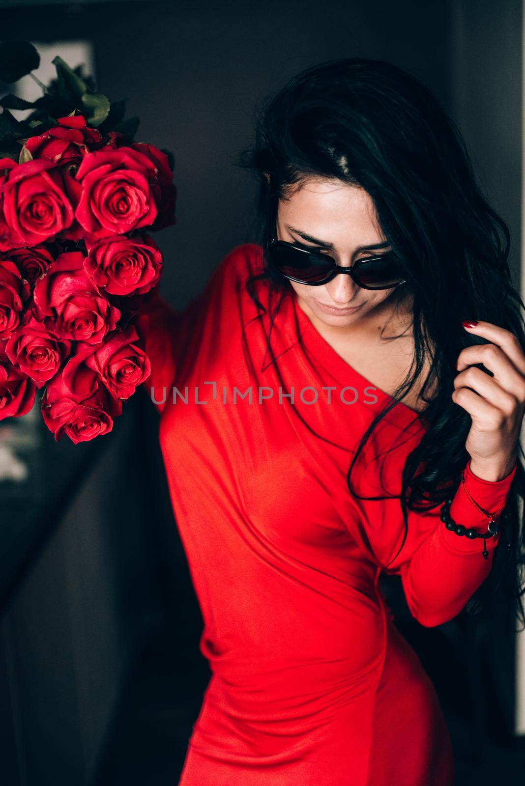 Charming young woman in red sexy dress and sunglasses posing with a bouquet of red roses. photo of a seductive woman with black hair. Selective focus, filmgrain by Ashtray25
