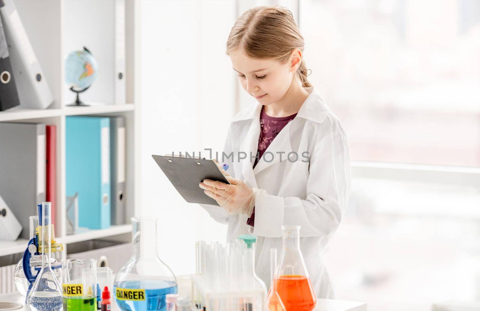 Girl during scientific chemistry experiment making notes close to table with tubes. Schoolgirl with chemical equipment on school lesson