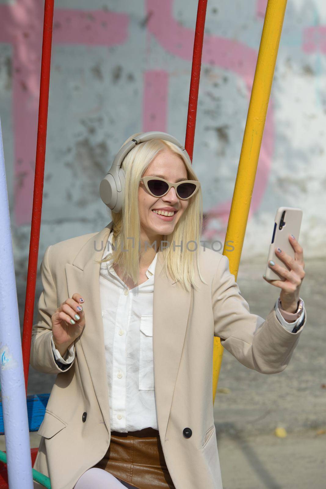 Young smiling cheerful woman outdoors using social media apps on phone for video chatting and stying connected. woman wearing white jacket, blouse, tights and brown leather skirt