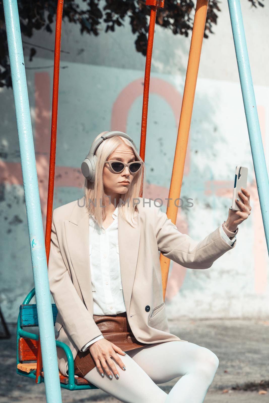 Young smiling cheerful woman outdoors using social media apps on phone for video chatting and stying connected. woman wearing white jacket, blouse, tights and brown leather skirt