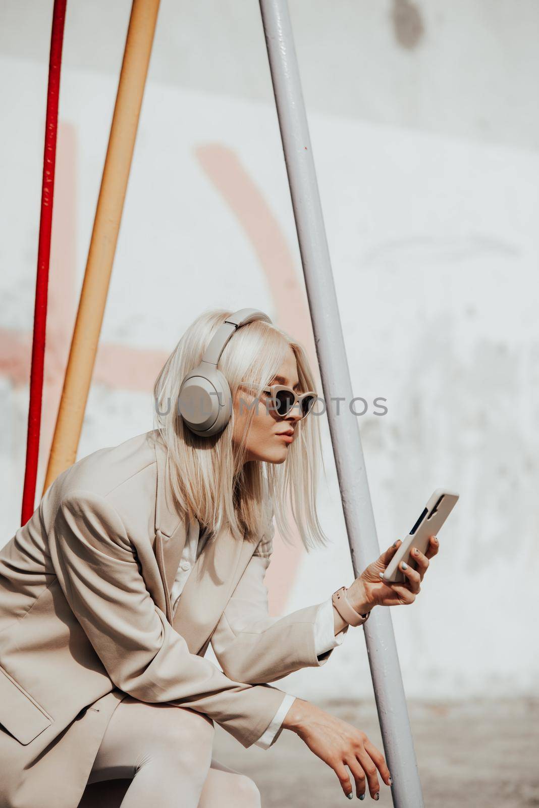 Portrait of blonde hipster fashion model wear stylish wireless headphones enjoy listen new cool music. woman wearing white jacket, blouse, tights and brown leather skirt