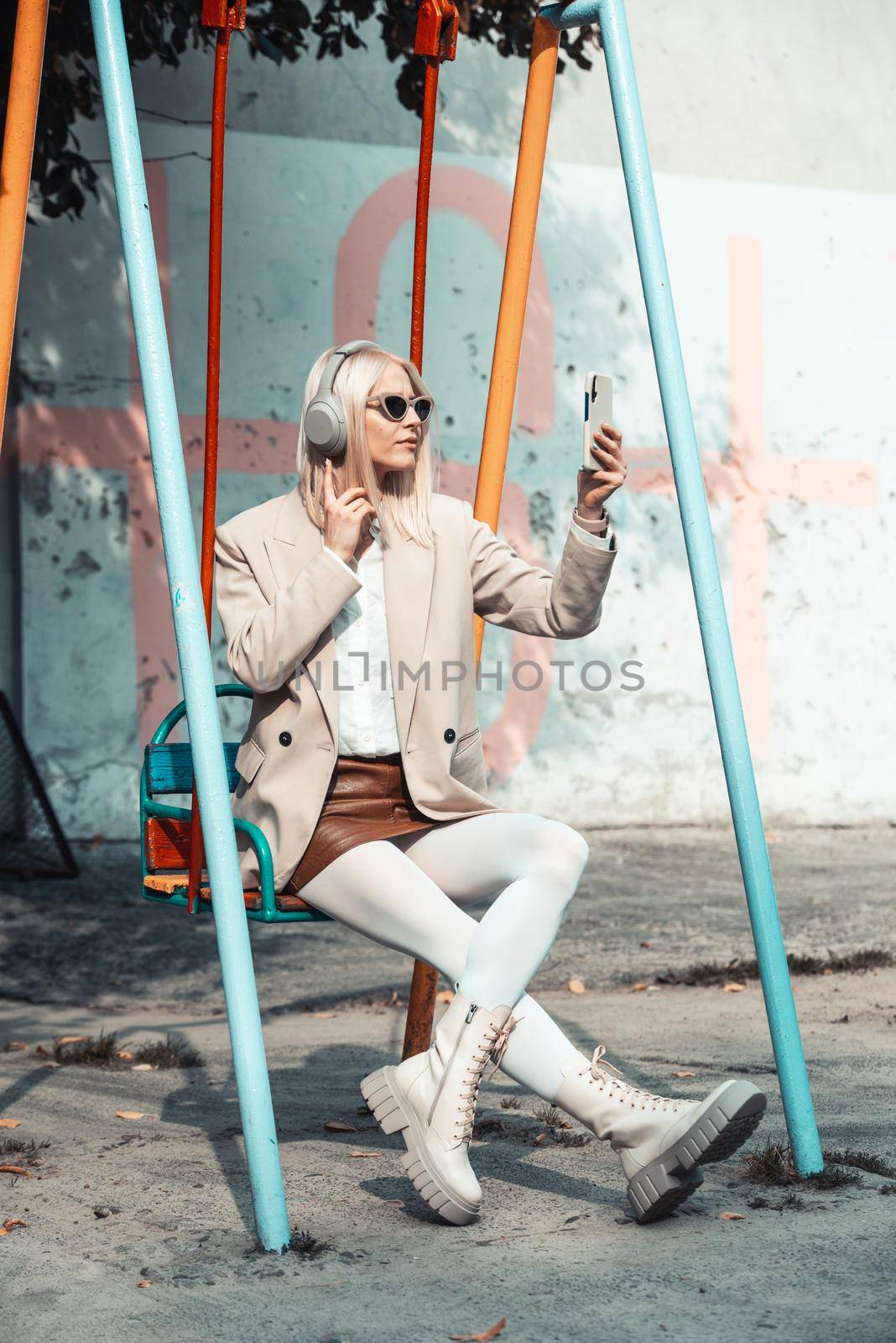 Young smiling cheerful woman outdoors using social media apps on phone for video chatting and stying connected. woman wearing white jacket, blouse, tights and brown leather skirt