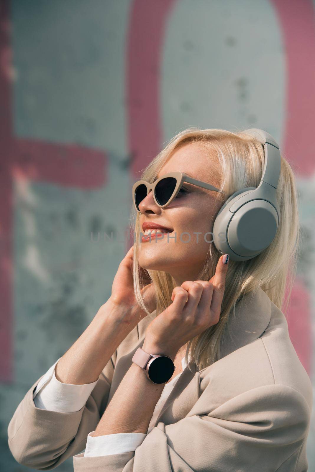 Portrait of blonde hipster fashion model wear stylish wireless headphones enjoy listen new cool music. woman wearing white jacket, blouse, tights and brown leather skirt