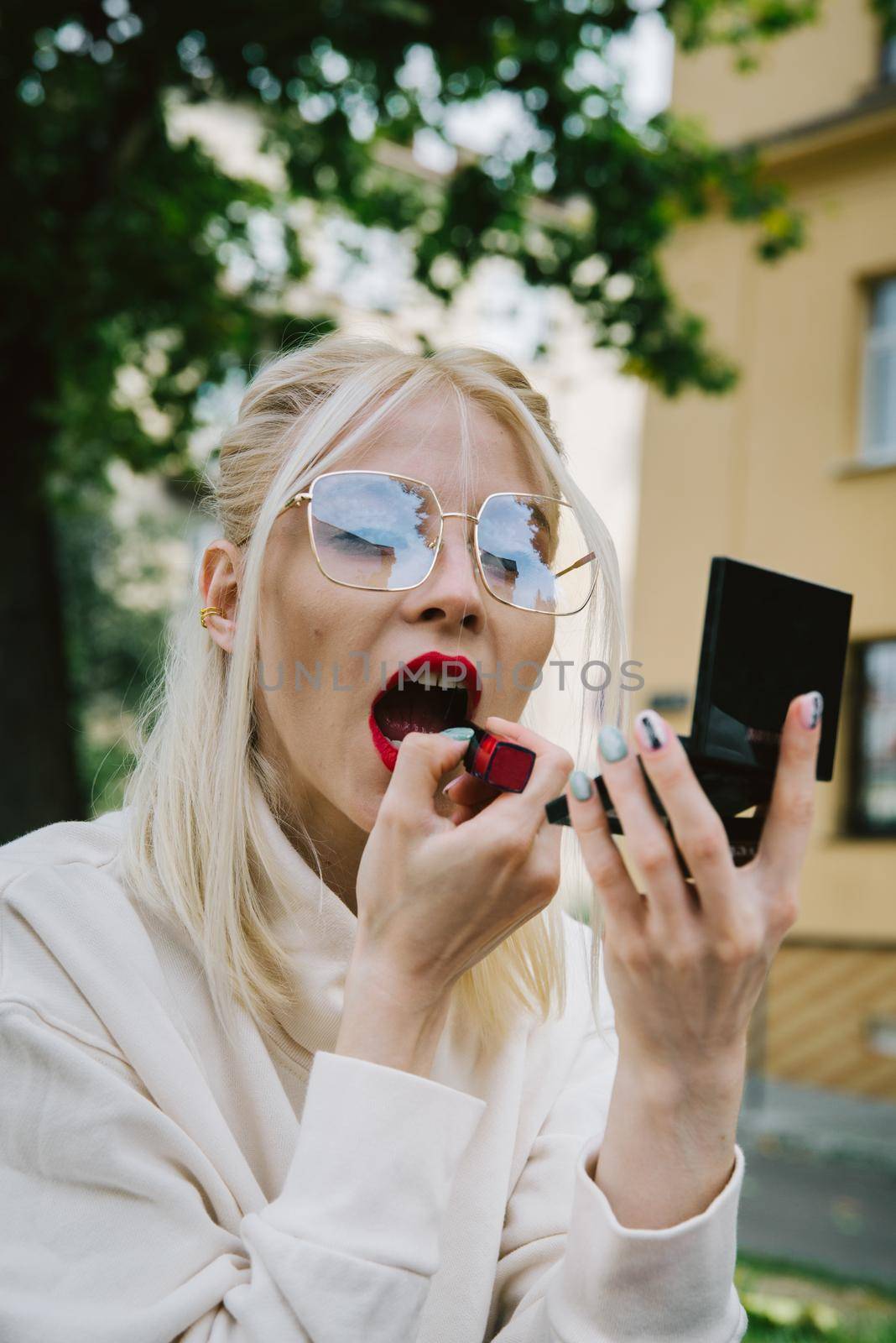 young smiling hipster happy woman doing make-up using lipstick and mirror outdoors by Ashtray25