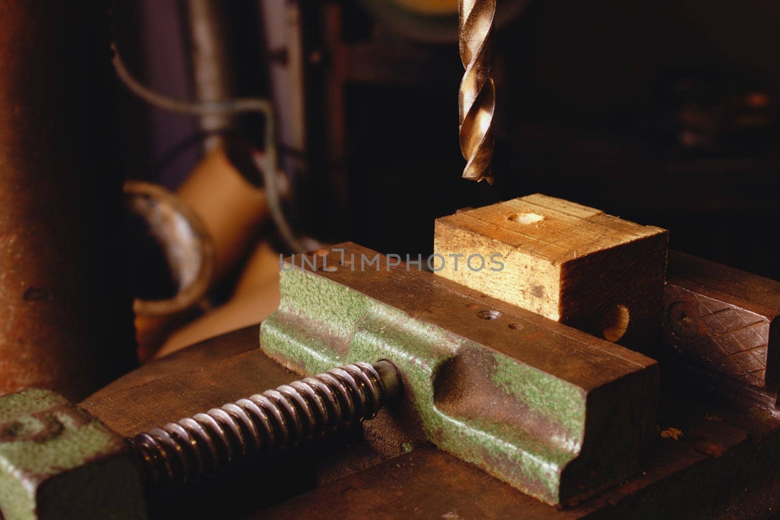 Drill bit coming down onto a piece of wood held in a vice in an industrial workshop