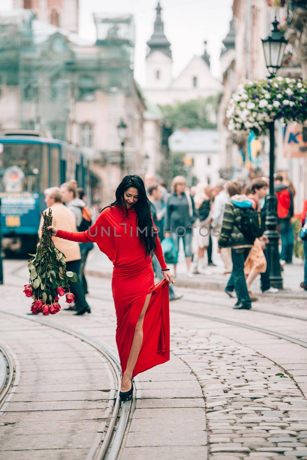 Charming young woman in red sexy dress posing with a bouquet of red roses. photo of a seductive woman with black hair on the city streets. Selective focus, filmgrain.