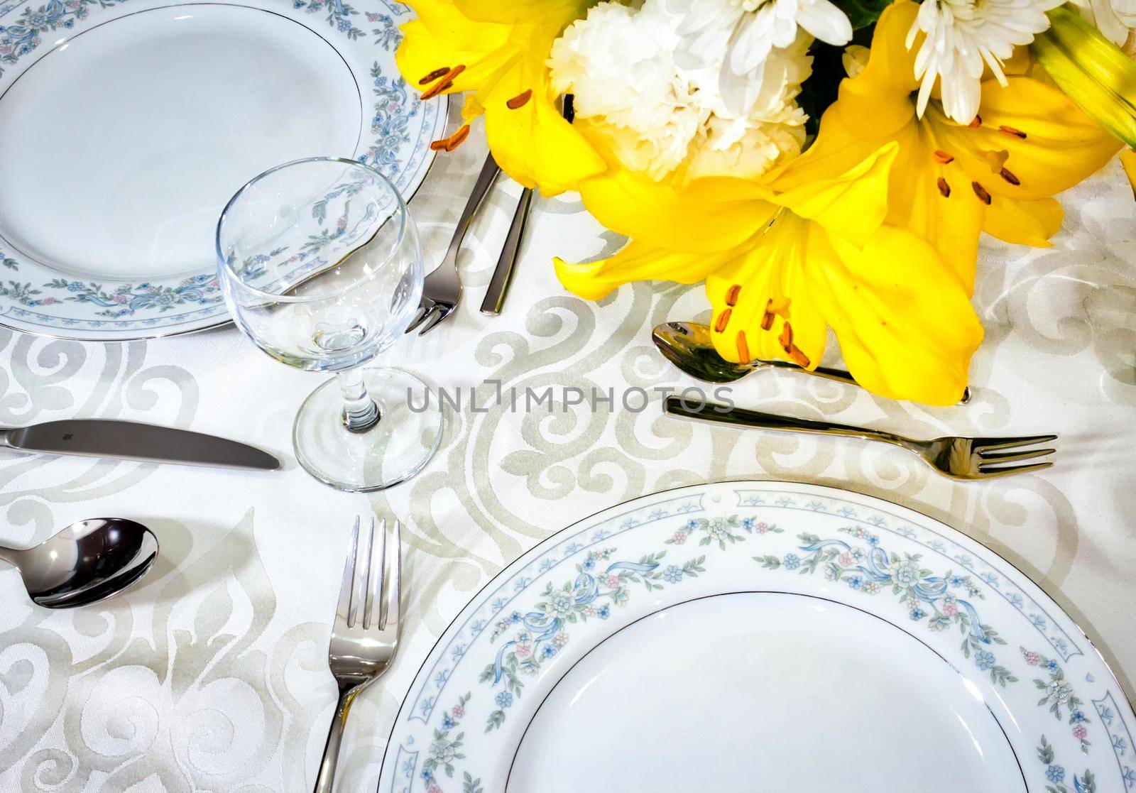 Elegant dining set for a romantic meal on a white tablecloth in a fancy restaurant with arranged flowers in a vase on the table