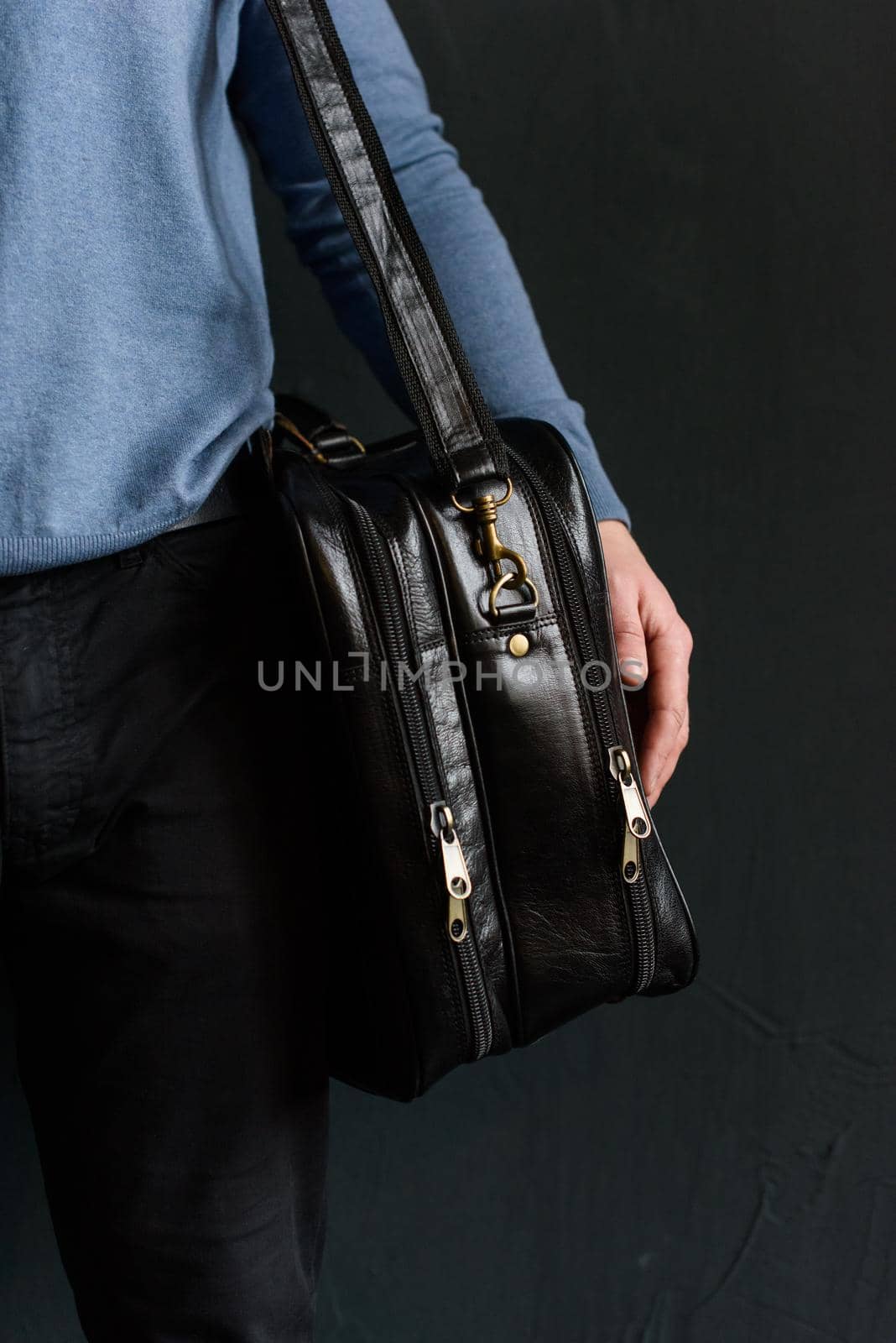 Man holding black leather travel bag. Soft light. Indoor photo