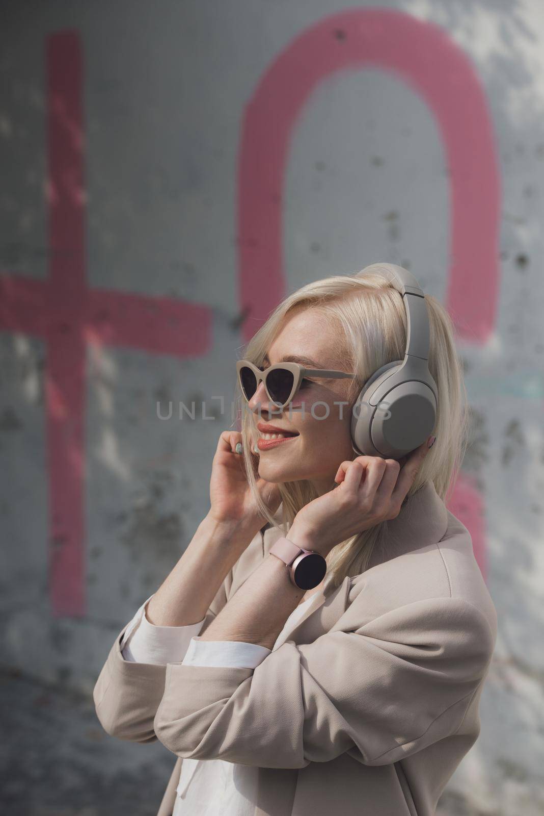 Portrait of blonde hipster fashion model wear stylish wireless headphones enjoy listen new cool music. woman wearing white jacket, blouse, tights and brown leather skirt