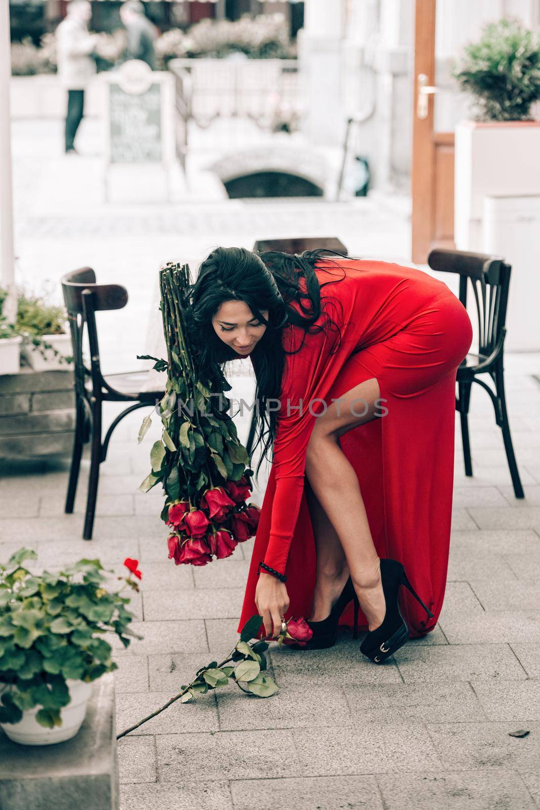 Charming young woman in red sexy dress posing with a bouquet of red roses. photo of a seductive woman with black hair on the city streets. Selective focus, filmgrain by Ashtray25