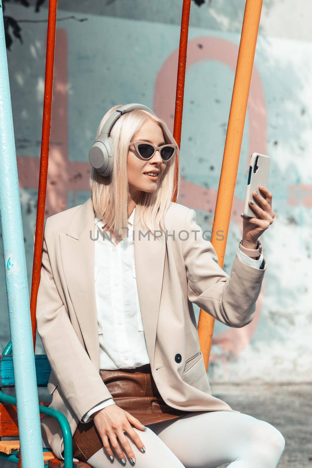 Young smiling cheerful woman outdoors using social media apps on phone for video chatting and stying connected. woman wearing white jacket, blouse, tights and brown leather skirt