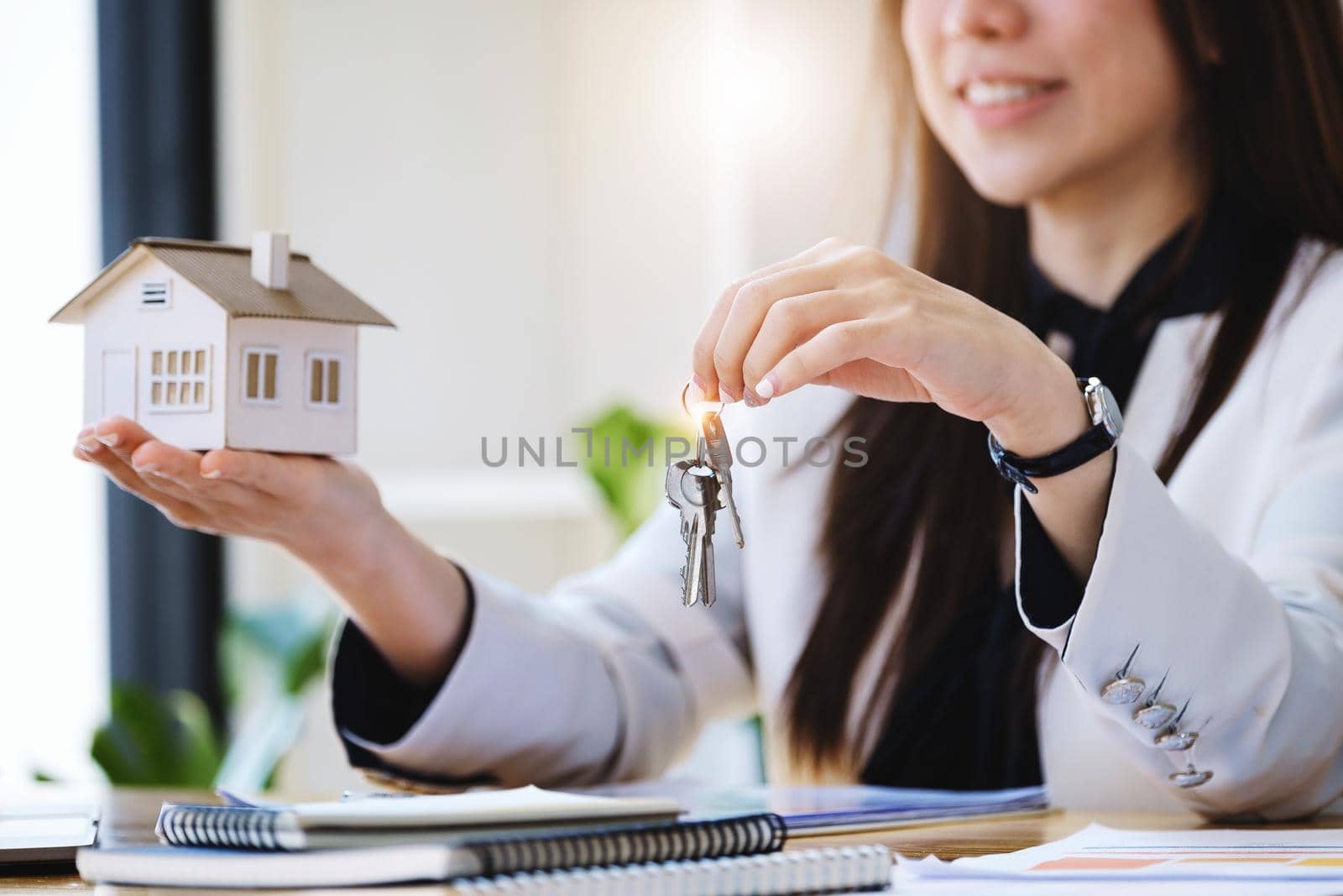 Accountant, businessman, real estate agent, Asian business woman handing house keys to customers along with house interest calculation documents for customers to sign