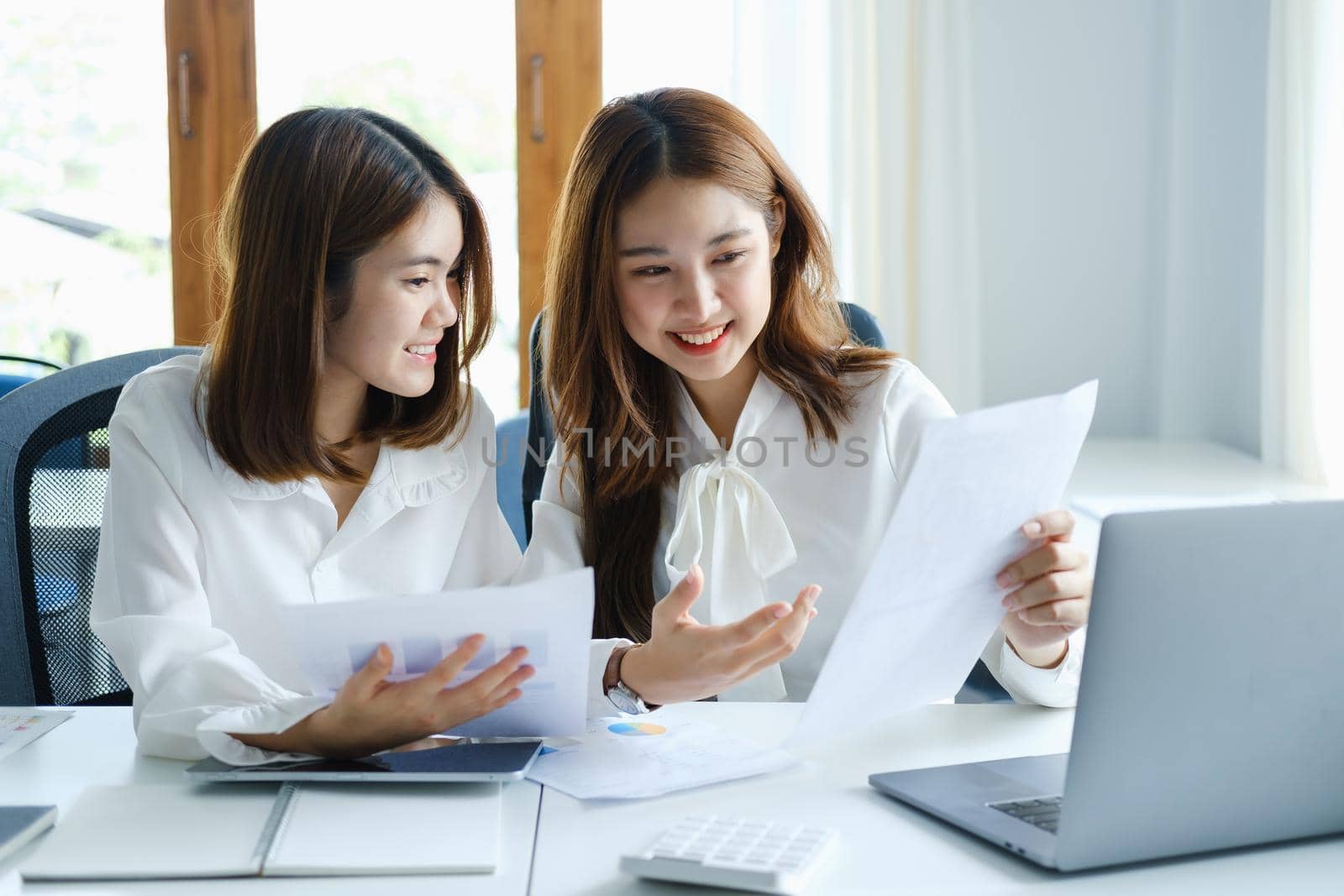 Consulting, learning, marketing, investment, finance, data analysis, research, two Asian women smiling and holding papers, sitting and analyzing financial statements and using computers at work
