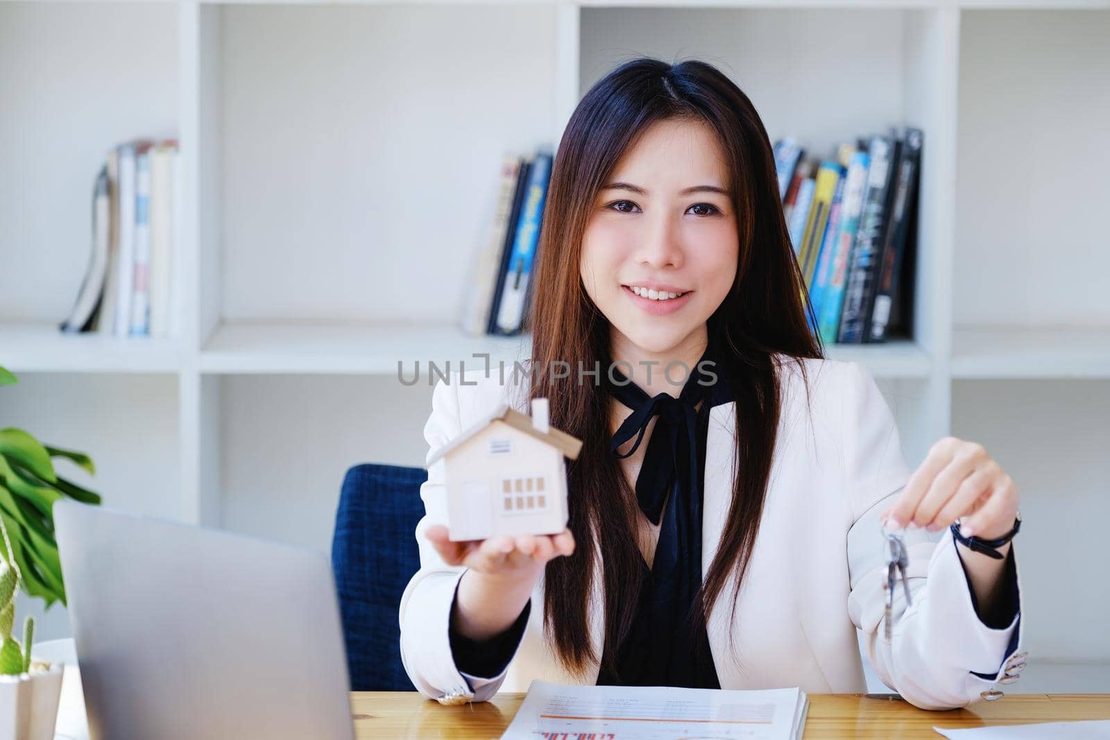 Accountant, businessman, real estate agent, Asian business woman handing house keys to customers along with house interest calculation documents for customers to sign. by Manastrong