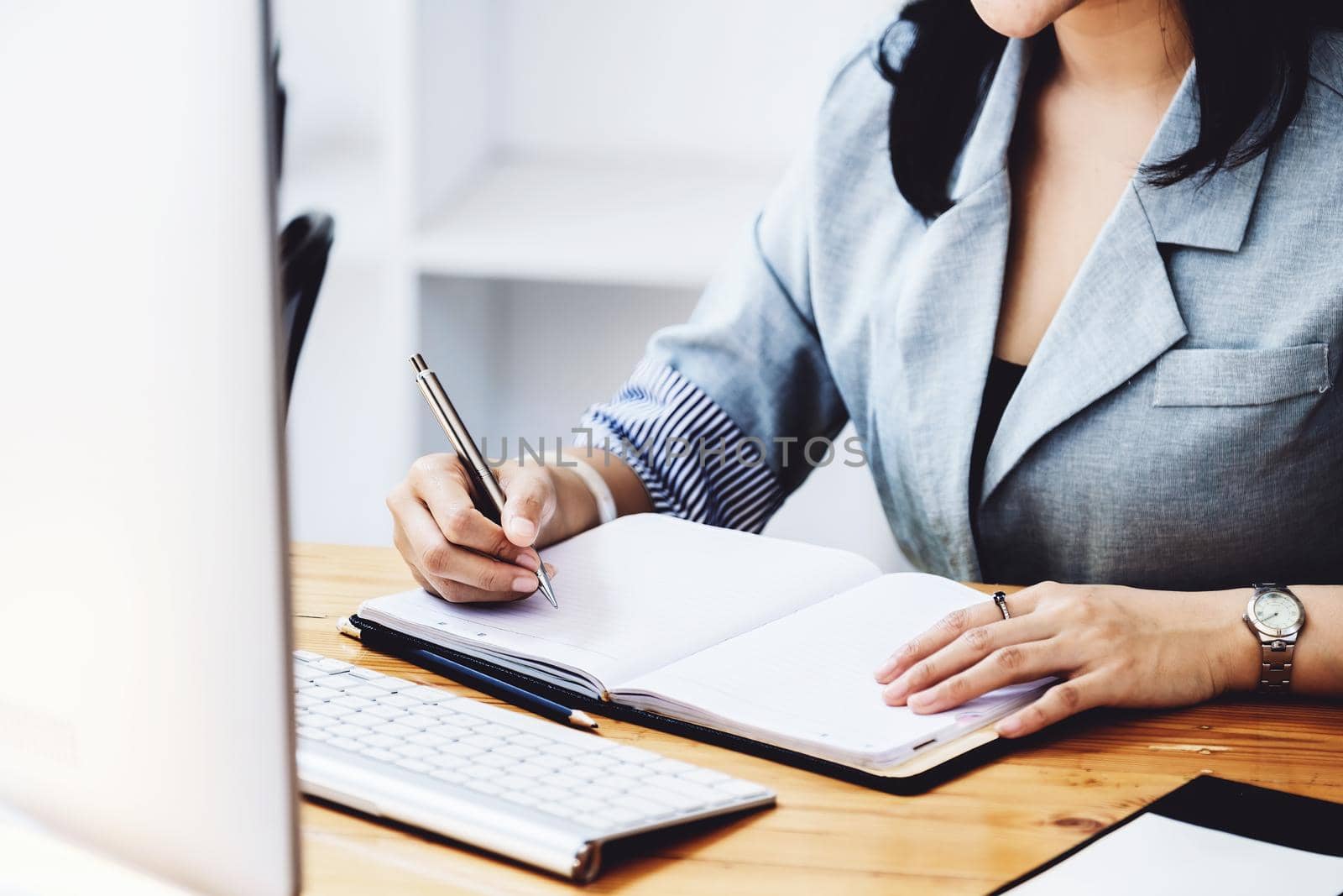 learning, note taking, planning, female employee holding a pen to write a notebook and using a computer to learn how to plan, invest and manage financial risks