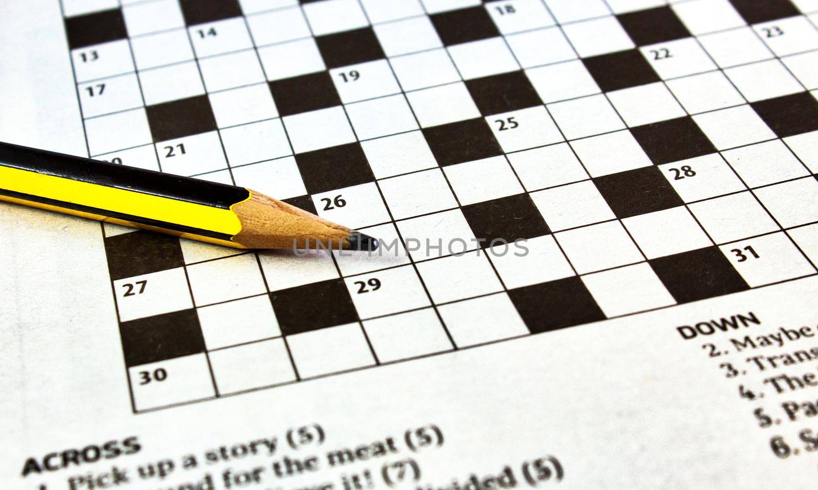 Closeup of crossword puzzle from a newspaper with a black and yellow lead pencil