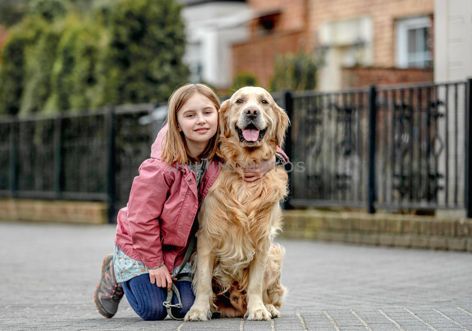 Preteen girl hugging golden retriever dog outdoors. Pretty child kid with purebred dog labrador sit on the ground happy