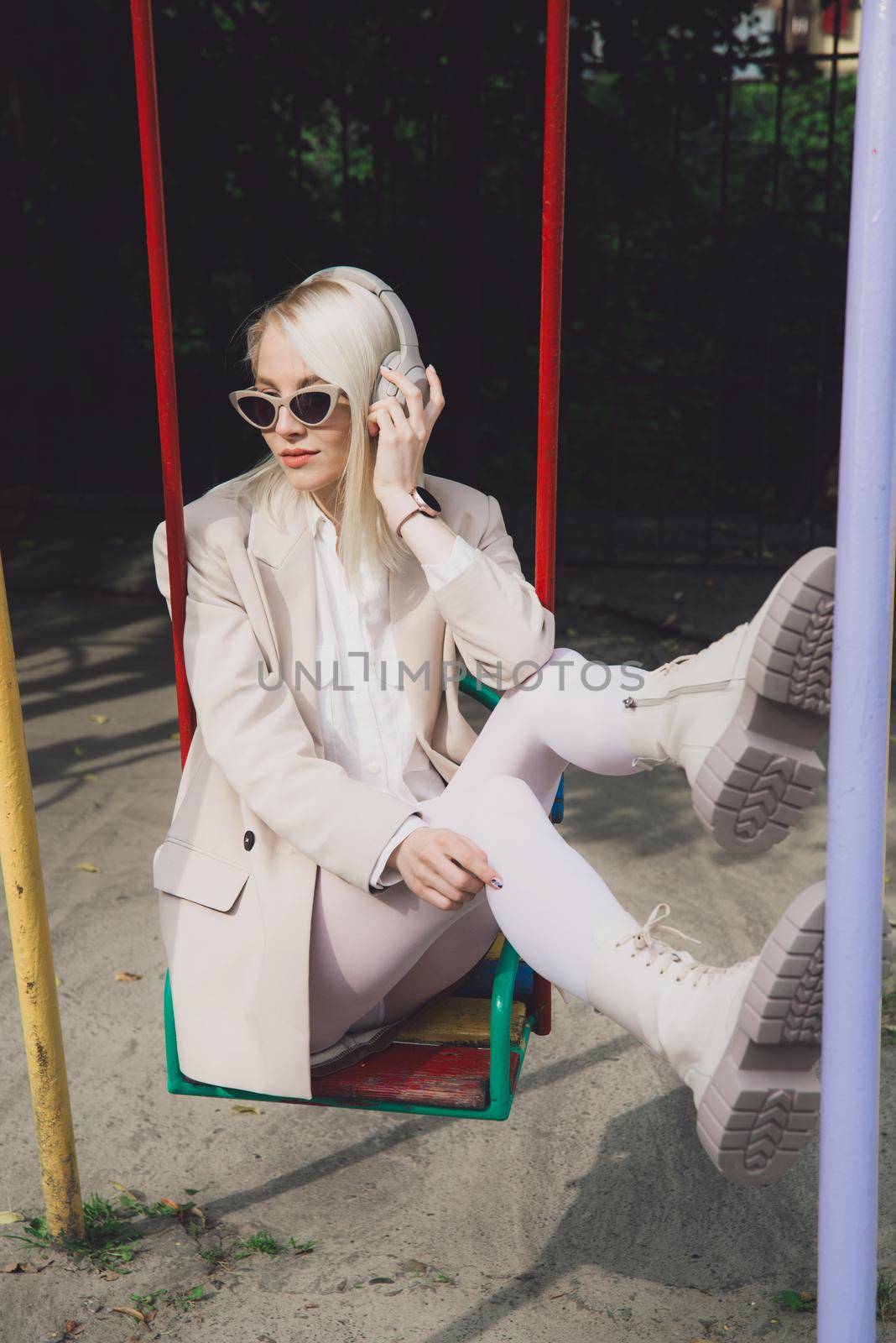 Portrait of blonde hipster fashion model wear stylish wireless headphones enjoy listen new cool music. woman wearing white jacket, blouse, tights and brown leather skirt