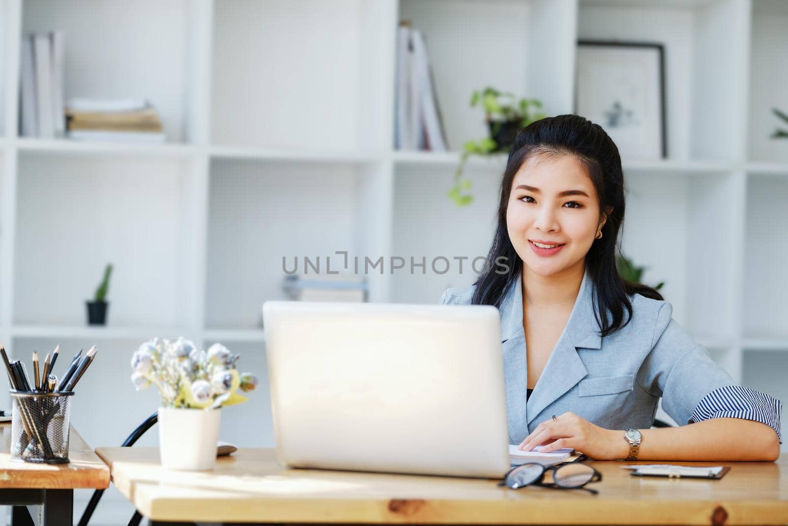 An Asian entrepreneur or businesswoman shows a smiling face while working with using computer on a wooden table. by Manastrong
