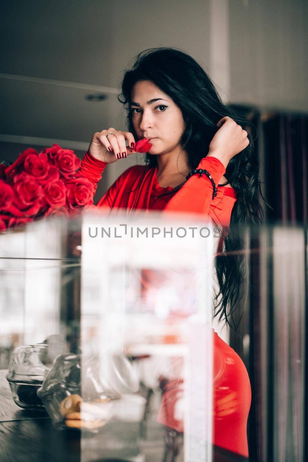Charming young woman in red sexy dress posing with a bouquet of red roses. photo of a seductive woman with black hair. Selective focus, filmgrain